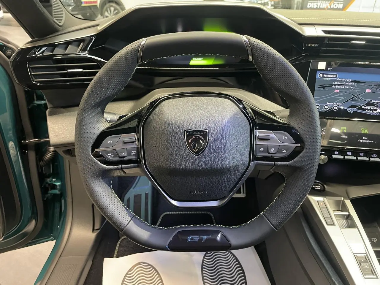 Vue rapprochée du volant GT en cuir noir avec surpiqûres vert Adamite dans l’habitacle bleu métallisé du Peugeot 308 2026.