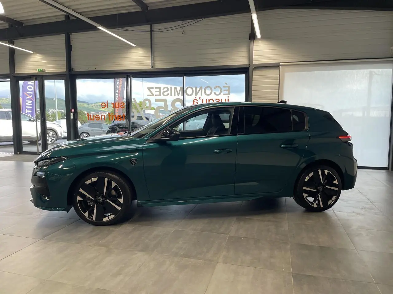 Profil droit de la Peugeot 308 GT bleu métallisé avec jantes alliage bi-tons et vitres surteintées en showroom.