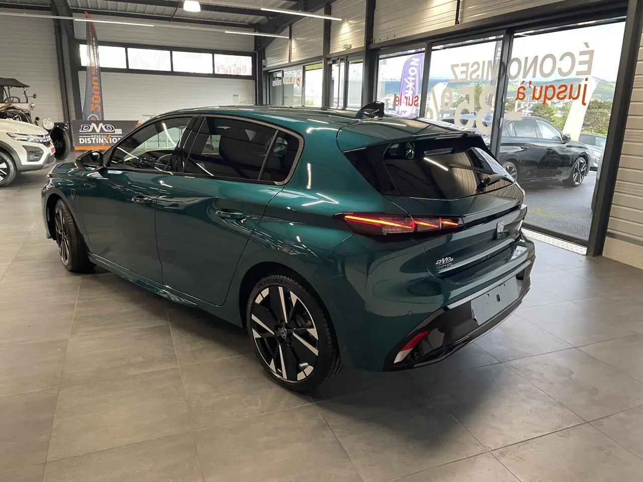 Peugeot 308 bleu métallisé vue 3/4 arrière droit en intérieur avec jantes alliage bi-tons et feux LED allumés.