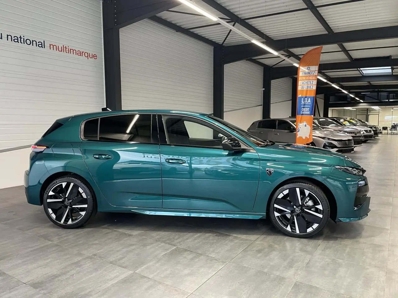 Vue latérale droite d'une Peugeot 308 GT 2026 bleu métallisé avec jantes alliage bi-tons et vitres surteintées en showroom.