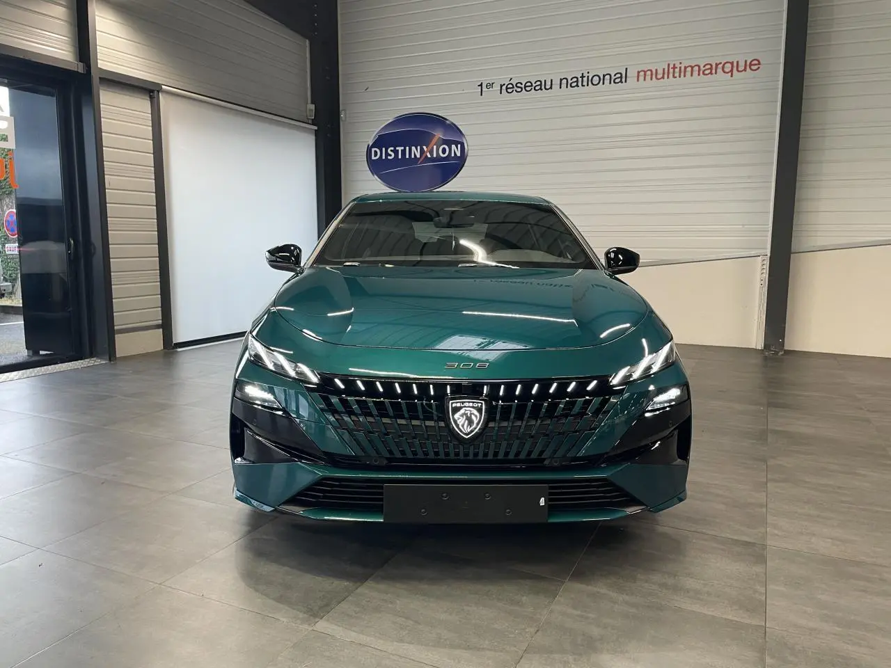 Vue frontale d'une Peugeot 308 2026 bleu métallisé avec calandre noire brillante et feux LED distinctifs.