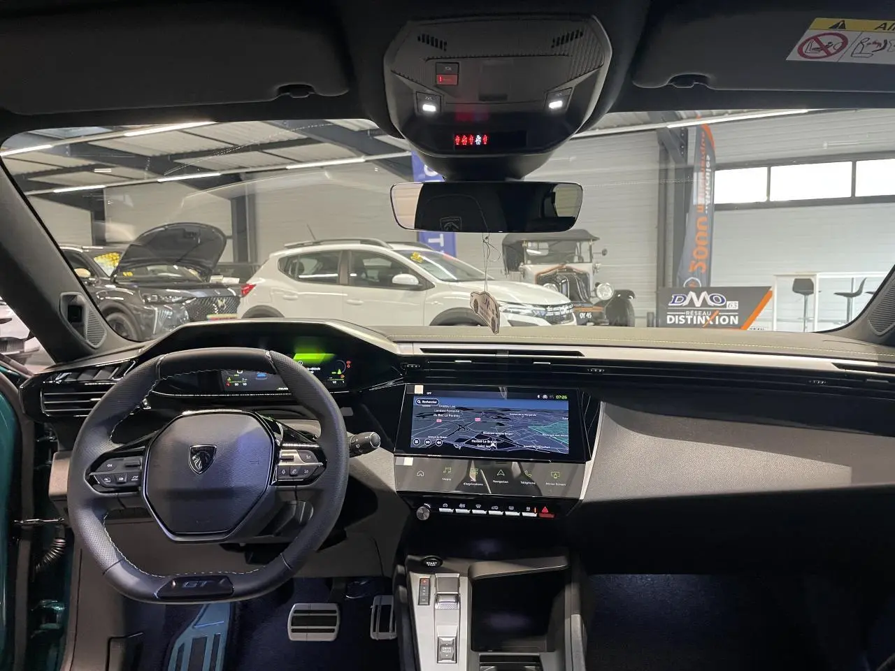 Vue intérieure avant du Peugeot 308 bleu, mettant en valeur le volant GT compact, l'écran tactile central et les pédaliers aluminium.