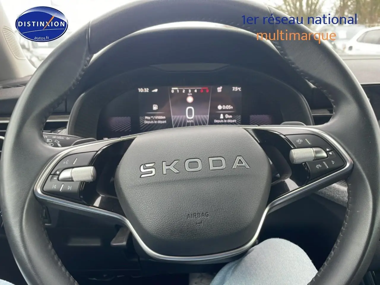 Vue rapprochée du volant cuir noir SKODA avec commandes multifonctions et tableau de bord numérique en arrière-plan.