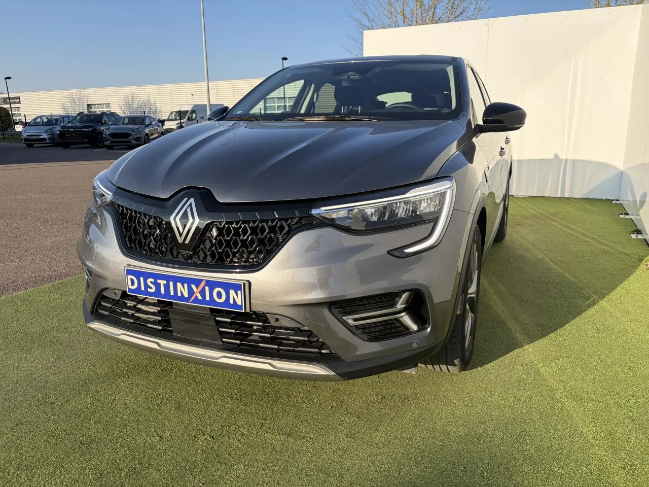 Renault Arkana gris métallisé vu de face droite, avec calandre noire et phares LED distinctifs.