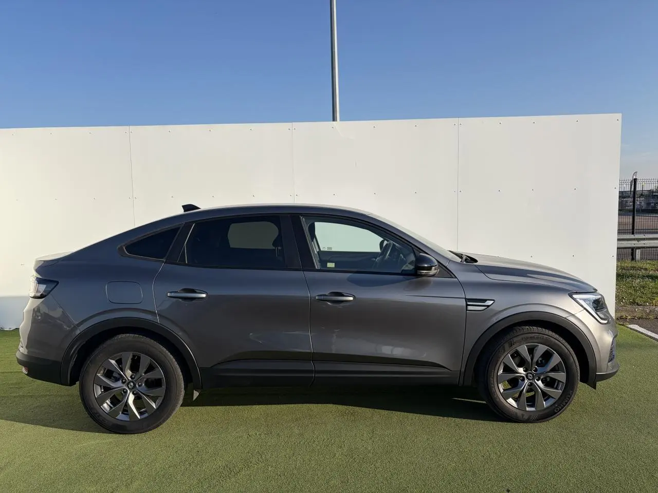 Profil droit d’un Renault Arkana gris métallisé 2025 avec jantes alliage et vitres surteintées.