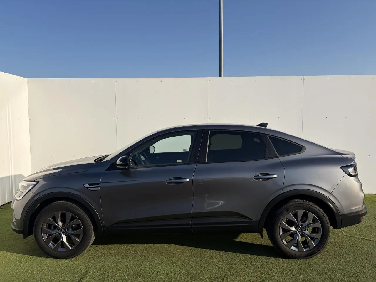 Profil côté gauche du Renault Arkana 2025 gris métallisé avec jantes alliage 17 pouces sur fond clair.