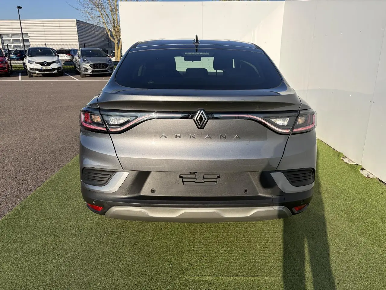 Vue arrière d’un Renault Arkana gris métallisé avec feux LED reliés et logo centré sur un parking.
