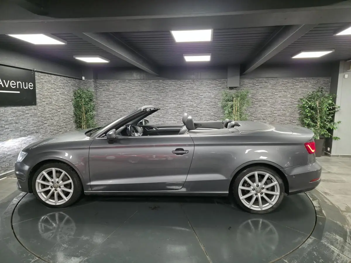 Audi A3 Cabriolet gris en profil droit, capote ouverte, jantes 10 branches et feux arrière allumés.