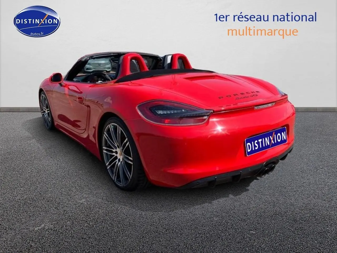 Vue 3/4 arrière droite d'une Porsche Boxster 981 rouge avec capote ouverte et jantes alu sport.