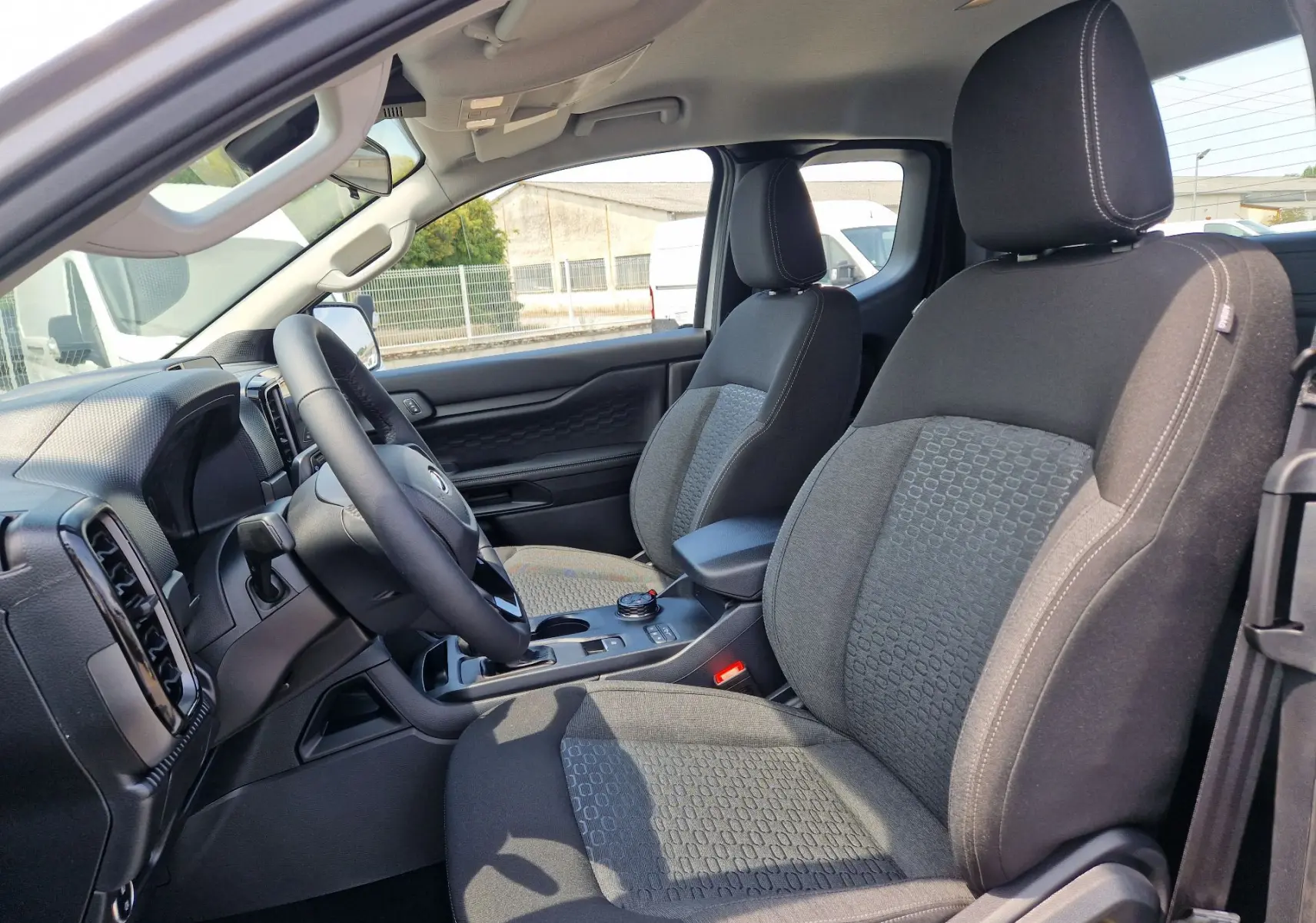 Vue intérieure côté conducteur du Ford Ranger Super Cabine 2026, sièges tissu gris avec console centrale et volant visibles.