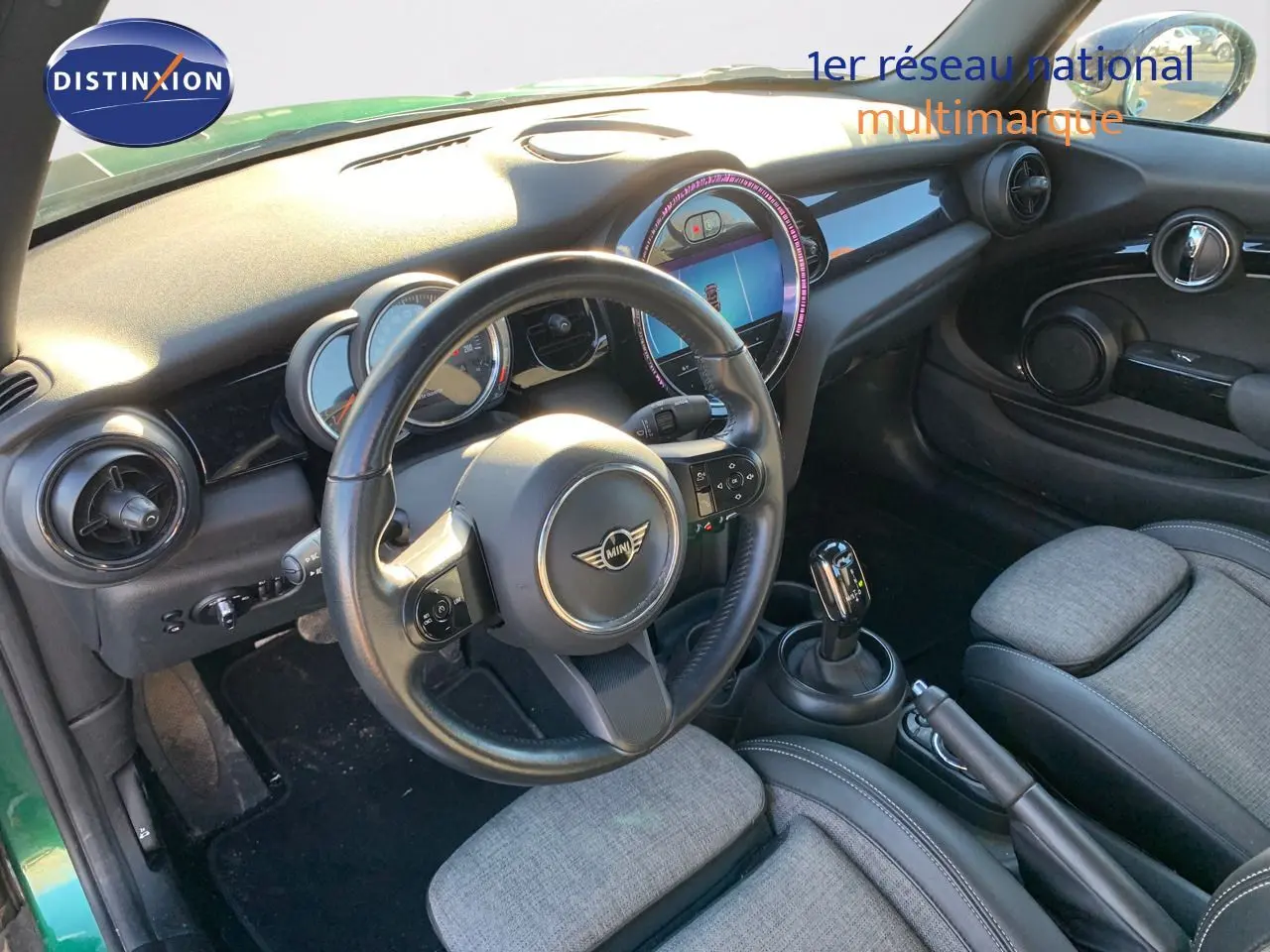 Intérieur de la MINI Cabriolet F57 2023 en British Racing Green, vue côté conducteur avec tableau de bord et volant visibles.