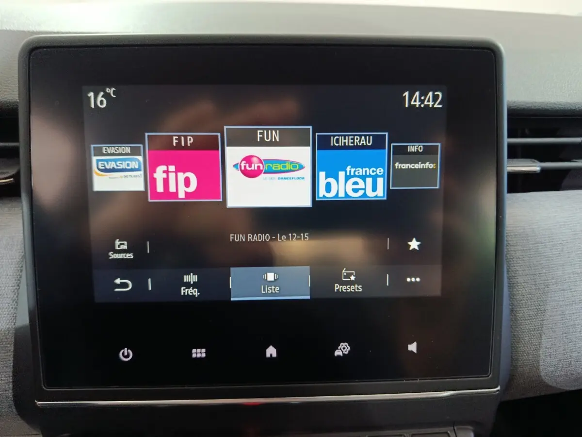 Écran tactile central de la Renault Clio gris clair, affichant les stations radio avec interface moderne.