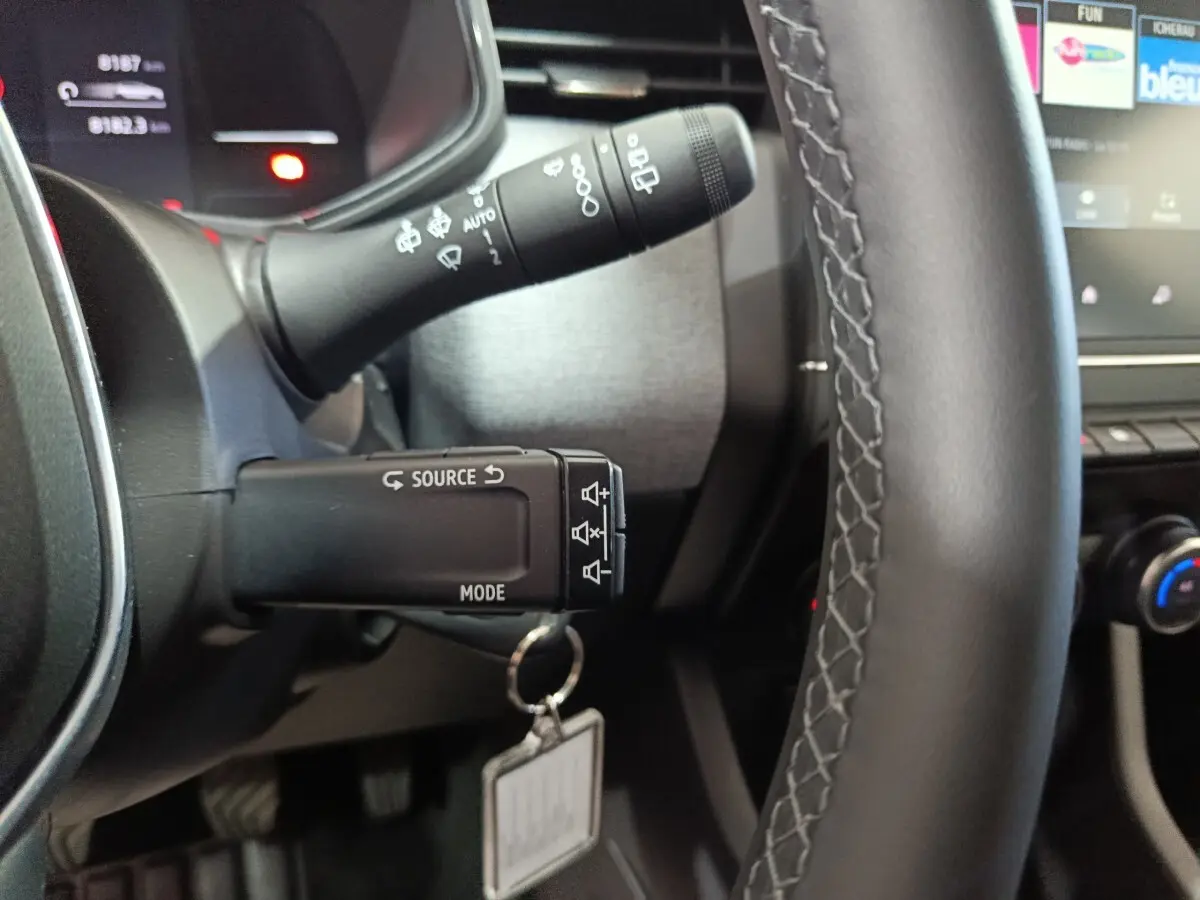 Gros plan sur le volant cuir synthétique et les commandes multifonctions à gauche du tableau de bord de la Renault Clio gris clair.