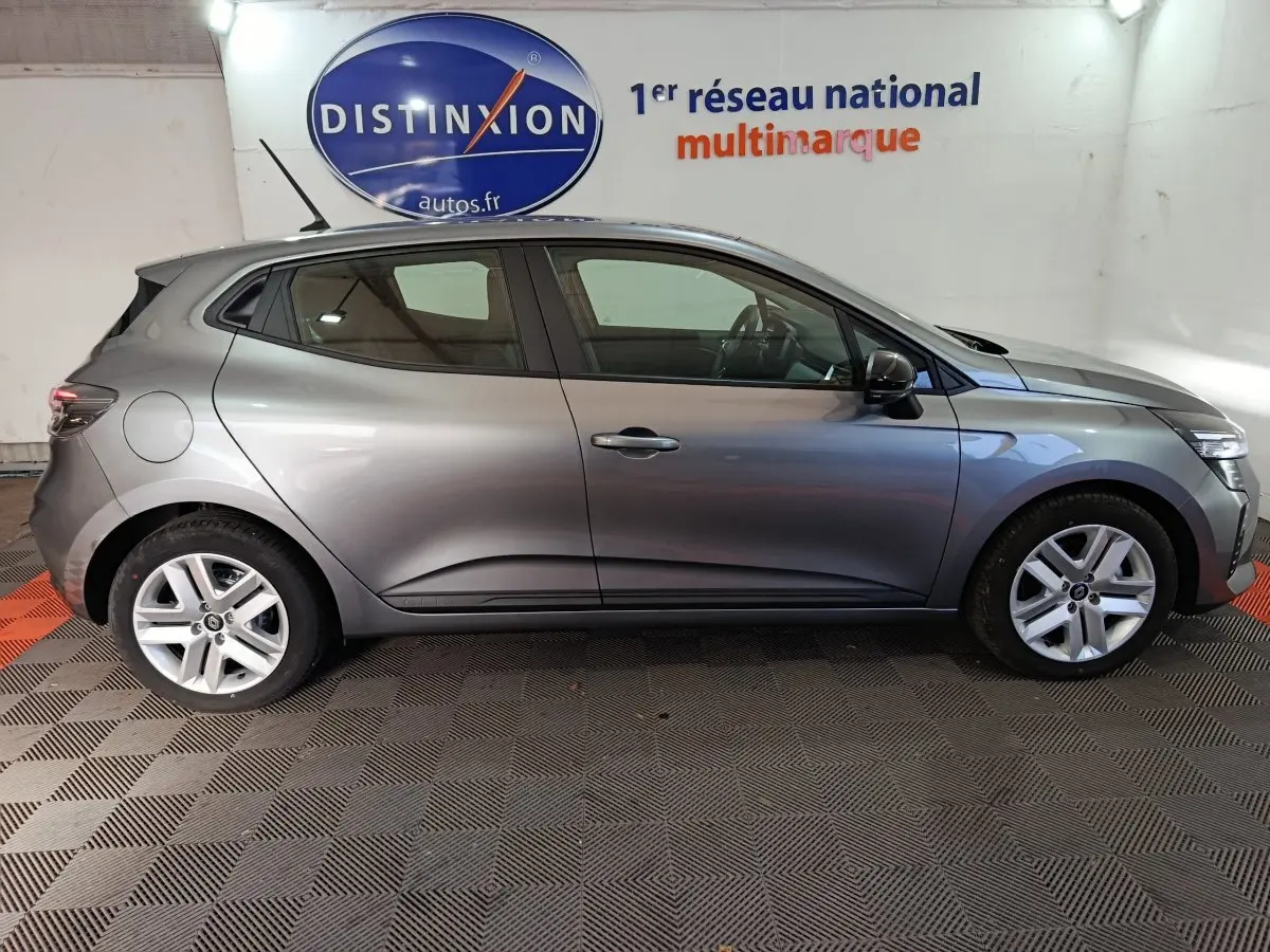 Profil côté gauche d'une Renault Clio gris clair Evolution Blue dCi 100 de 2025, en intérieur sur sol damier.
