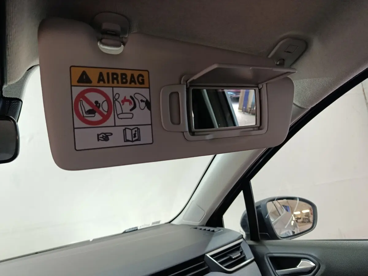 Vue intérieure côté conducteur de la Renault Clio gris clair 2025, pare-soleil avec miroir et avertissement airbag visible.