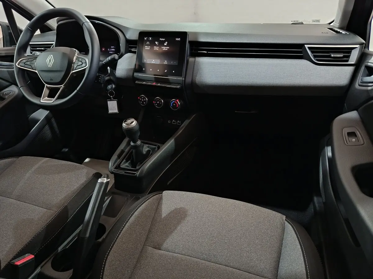 Vue intérieure avant droite de la Renault Clio 2025, tableau de bord gris clair avec écran tactile et volant multifonctions cuir synthétique.
