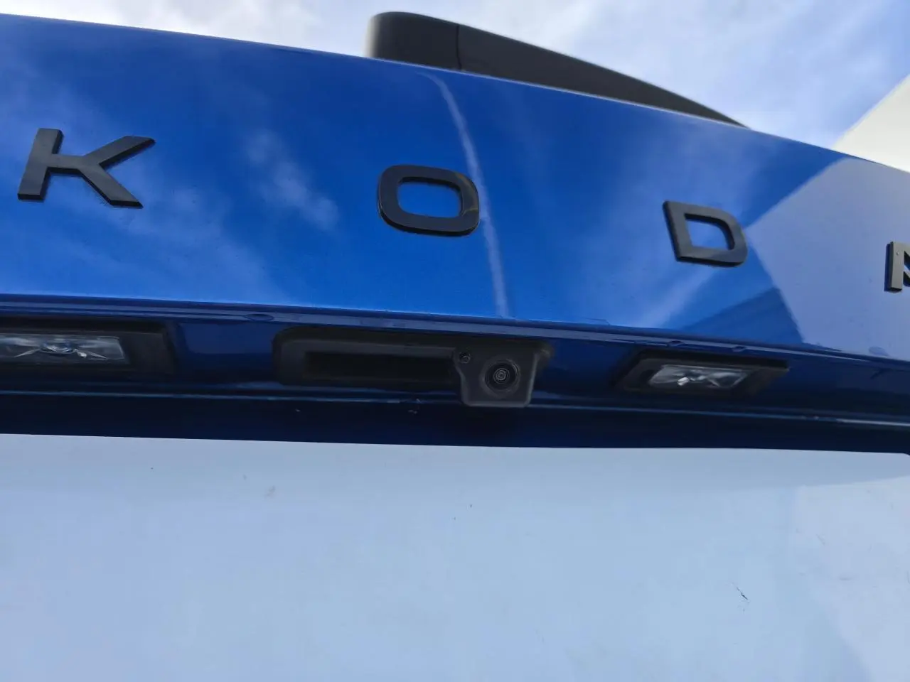 Gros plan sur la caméra de recul intégrée au hayon bleu racing avec lettres noires SKODA, toit noir visible en haut.