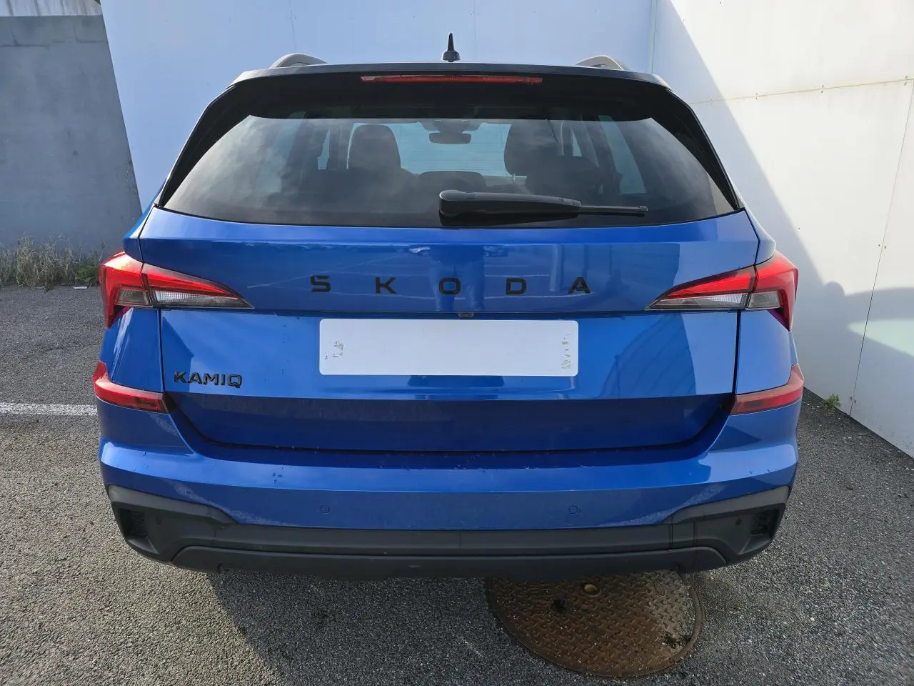 Vue arrière d'un Skoda Kamiq bleu racing avec toit noir et feux arrière LED distinctifs.