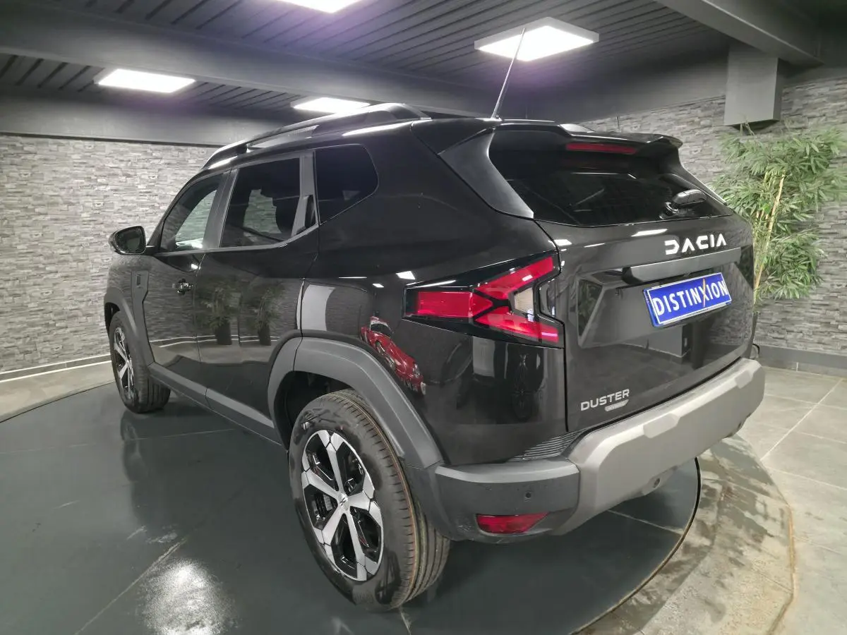Vue 3/4 arrière droite du Dacia Duster 1.6 Hybrid noir nacré avec jantes alliage et barres de toit noires.