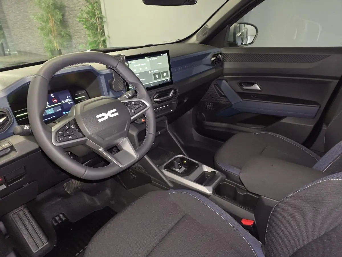 Vue intérieure côté conducteur du Dacia Duster 1.6 Hybrid 2025, tableau de bord et volant noir avec inserts Denim Bleu.