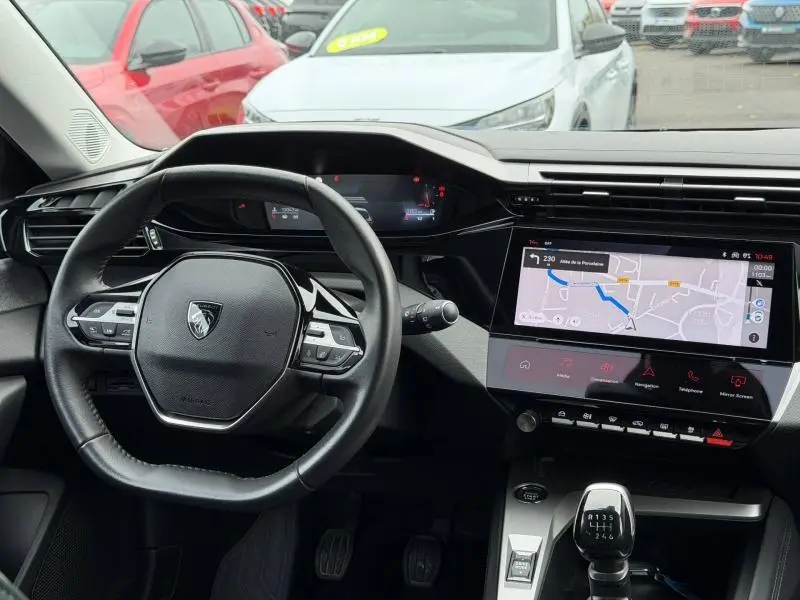Vue intérieure du poste de conduite de la Peugeot 308 2024 gris, avec volant multifonction et écran tactile de navigation.