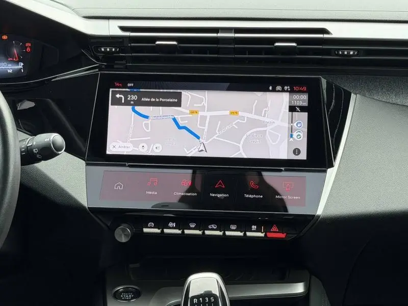 Vue intérieure du tableau de bord de la Peugeot 308 2024 gris, avec écran tactile affichant la navigation et levier de vitesse manuel.