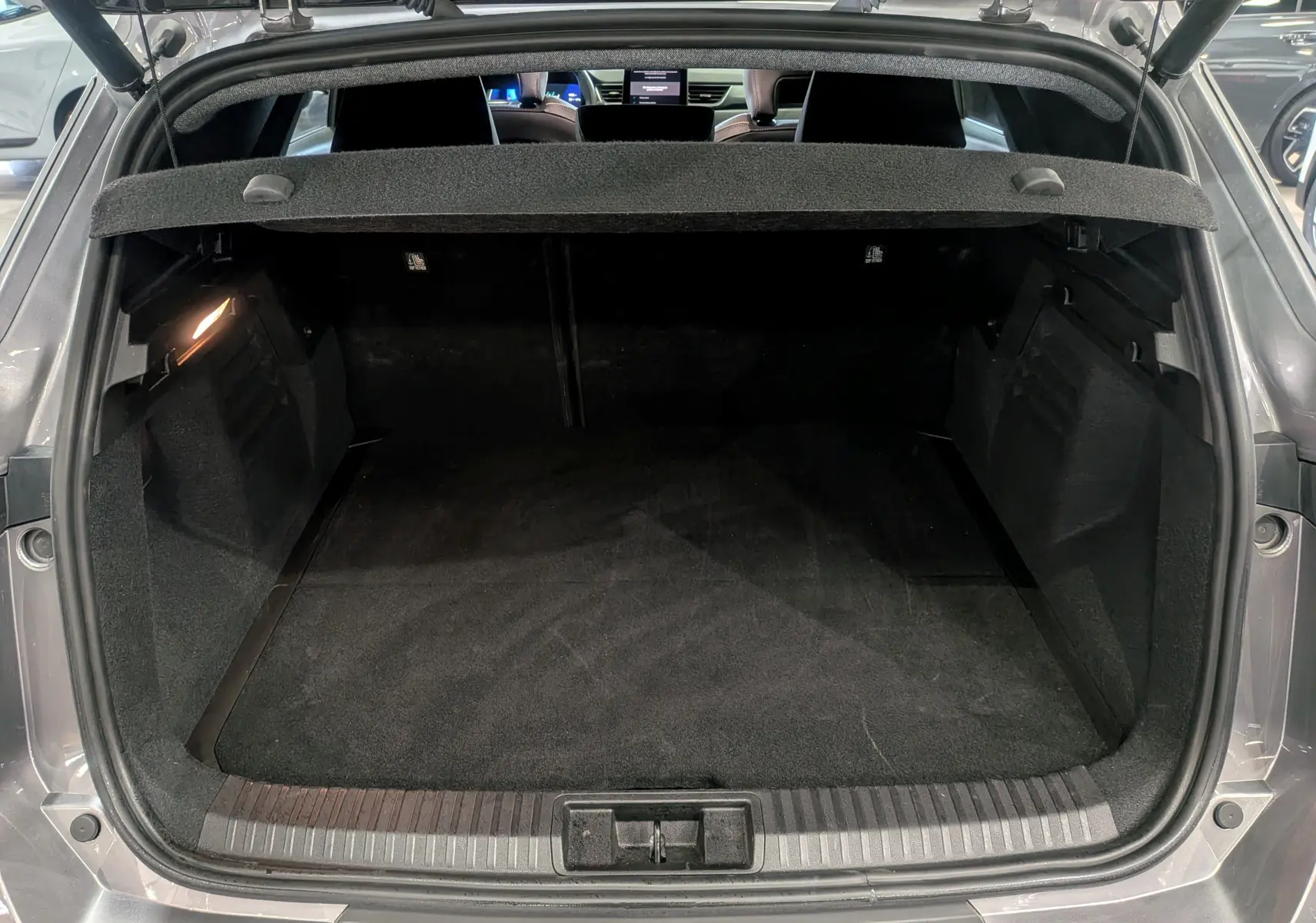 Coffre ouvert vu de l'arrière d'une Renault Symbioz gris Cassiopé, intérieur noir et tablette cache-bagages visible.