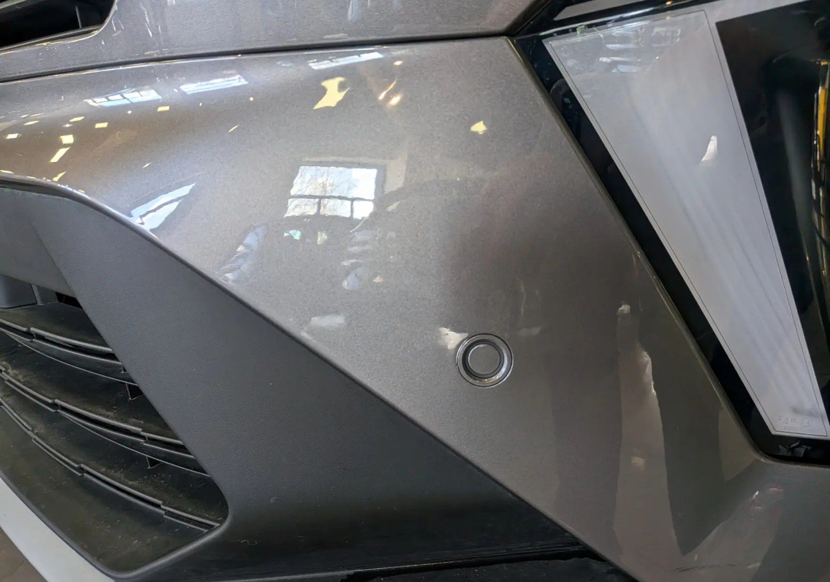 Gros plan sur l'avant droit gris Cassiopé du Renault SYMBIOZ 2025, mettant en valeur le capteur de stationnement et le phare LED.