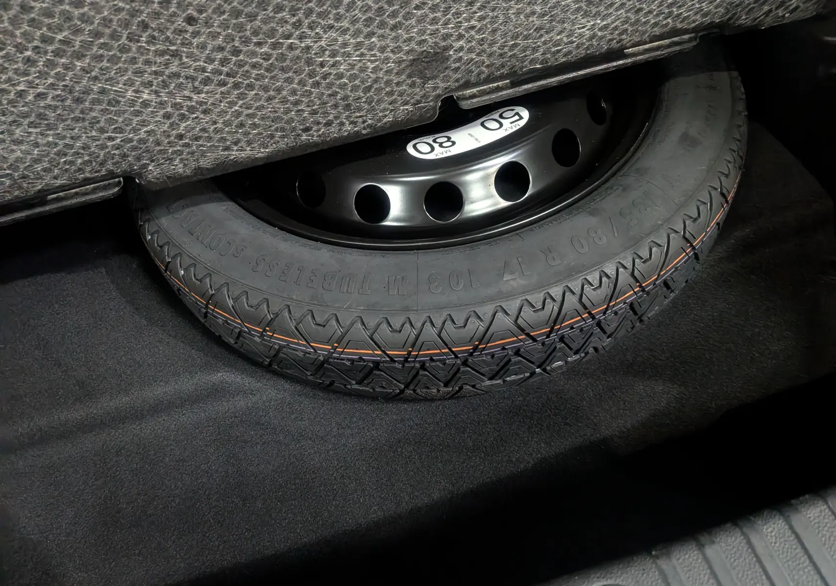 Roue de secours noire avec pneu neuf, vue en gros plan dans le coffre d’un Renault Symbioz gris Cassiopé.