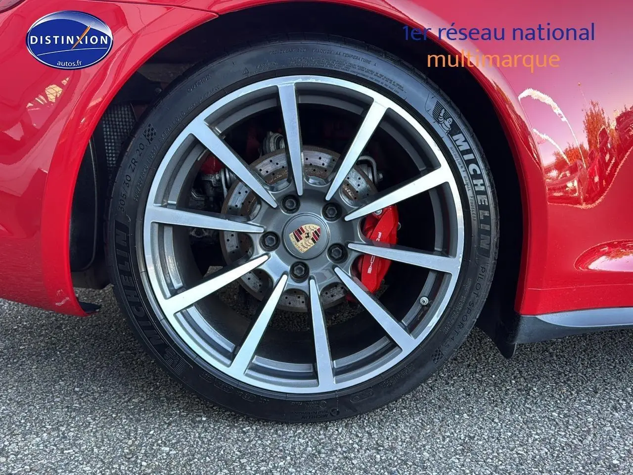Gros plan sur la jante alu grise et le frein rouge d’une Porsche 911 Carrera 4 rouge côté arrière droit.