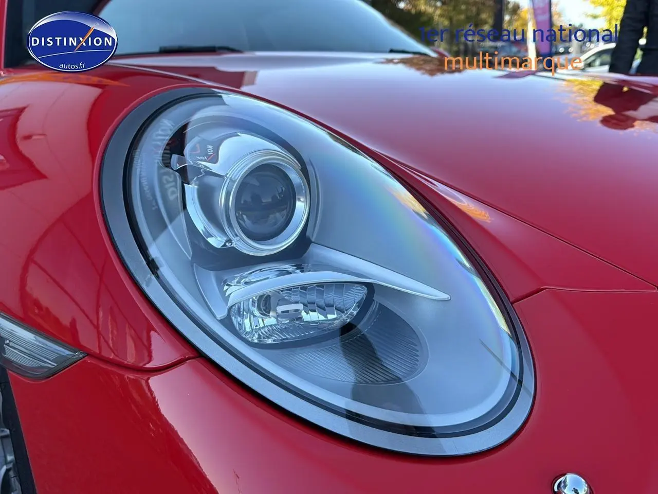 Gros plan sur le phare avant gauche d’une Porsche 911 rouge (991) Carrera 4 PDK de 2013 avec carrosserie brillante.