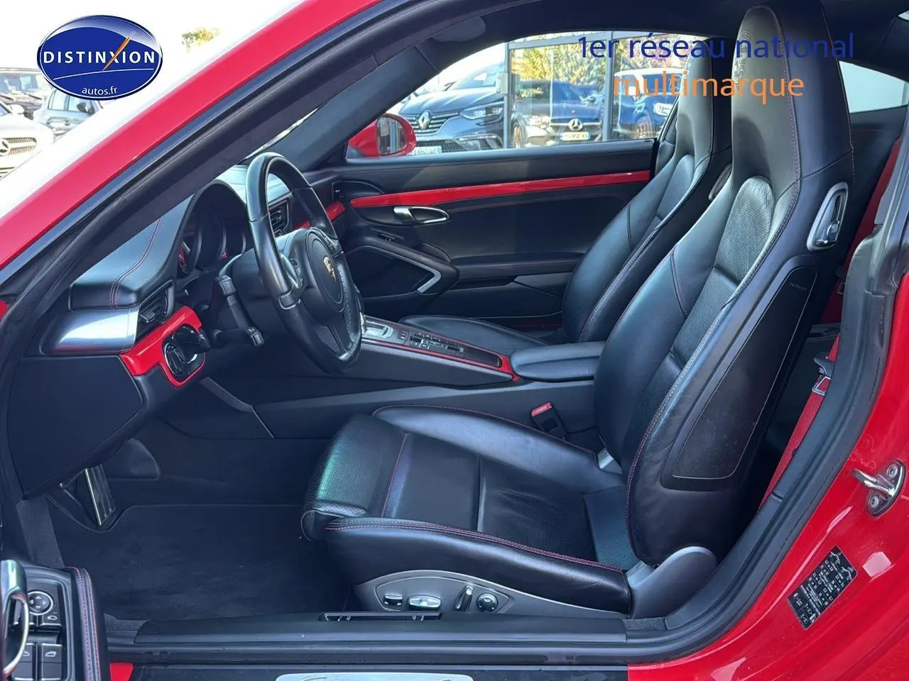 Vue intérieure côté conducteur d'une Porsche 911 rouge avec sièges cuir noirs et détails rouges sur tableau de bord.