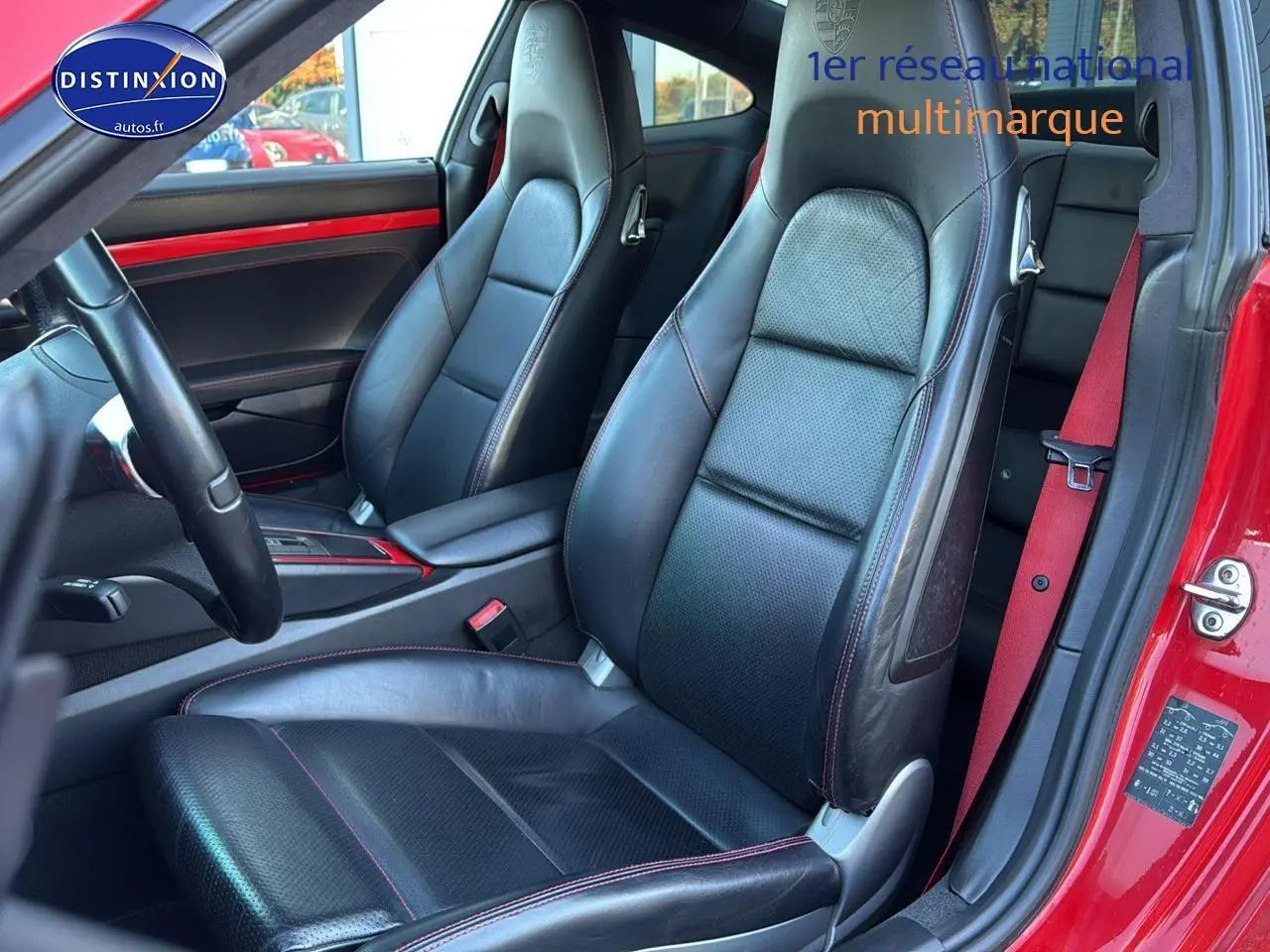 Vue intérieure côté conducteur de la Porsche 911 rouge, sièges cuir noir avec surpiqûres rouges et ceinture rouge visible.