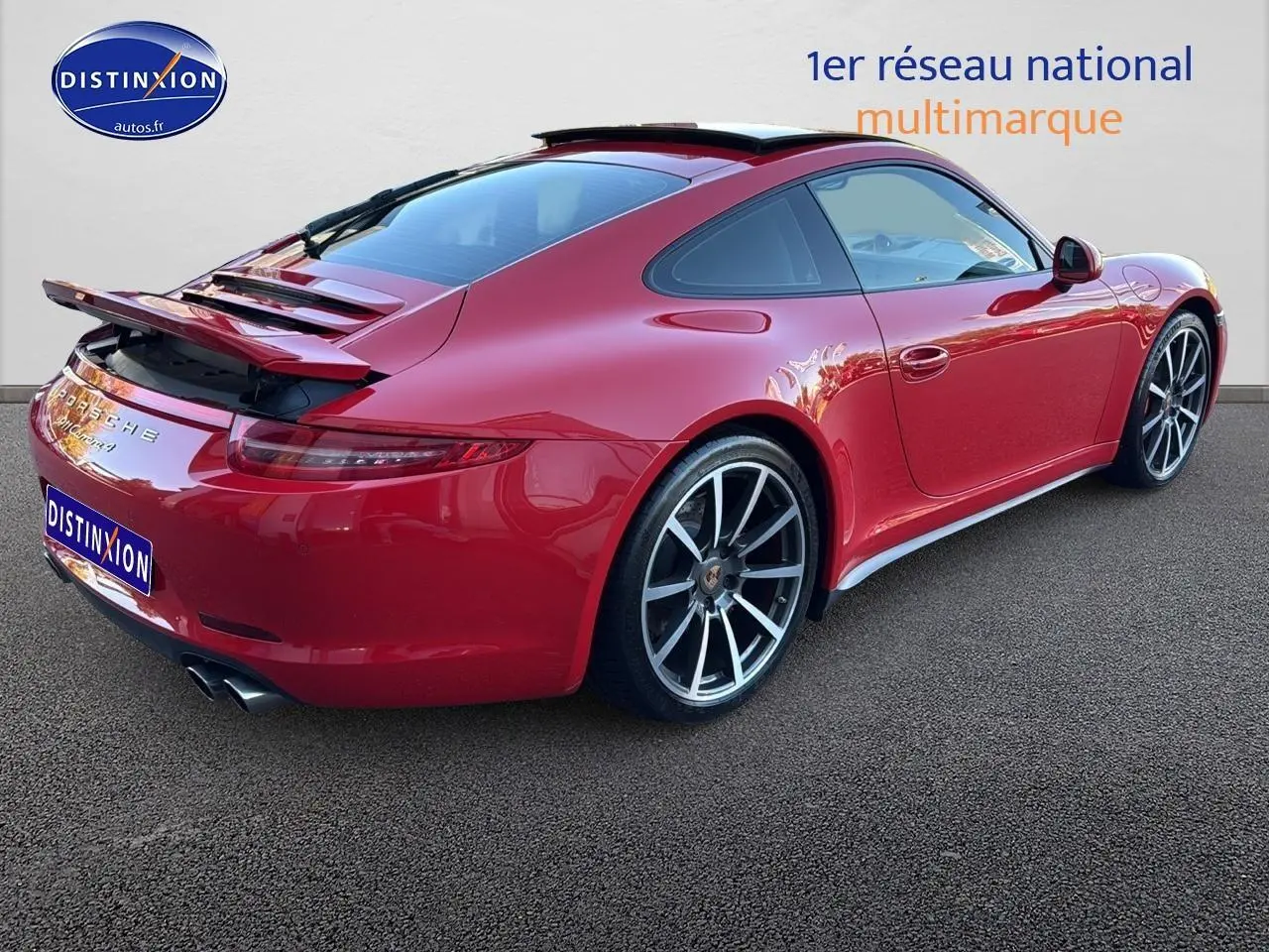 Vue 3/4 arrière droite d'une Porsche 911 (991) Carrera 4 PDK rouge avec becquet arrière relevé et jantes alu.