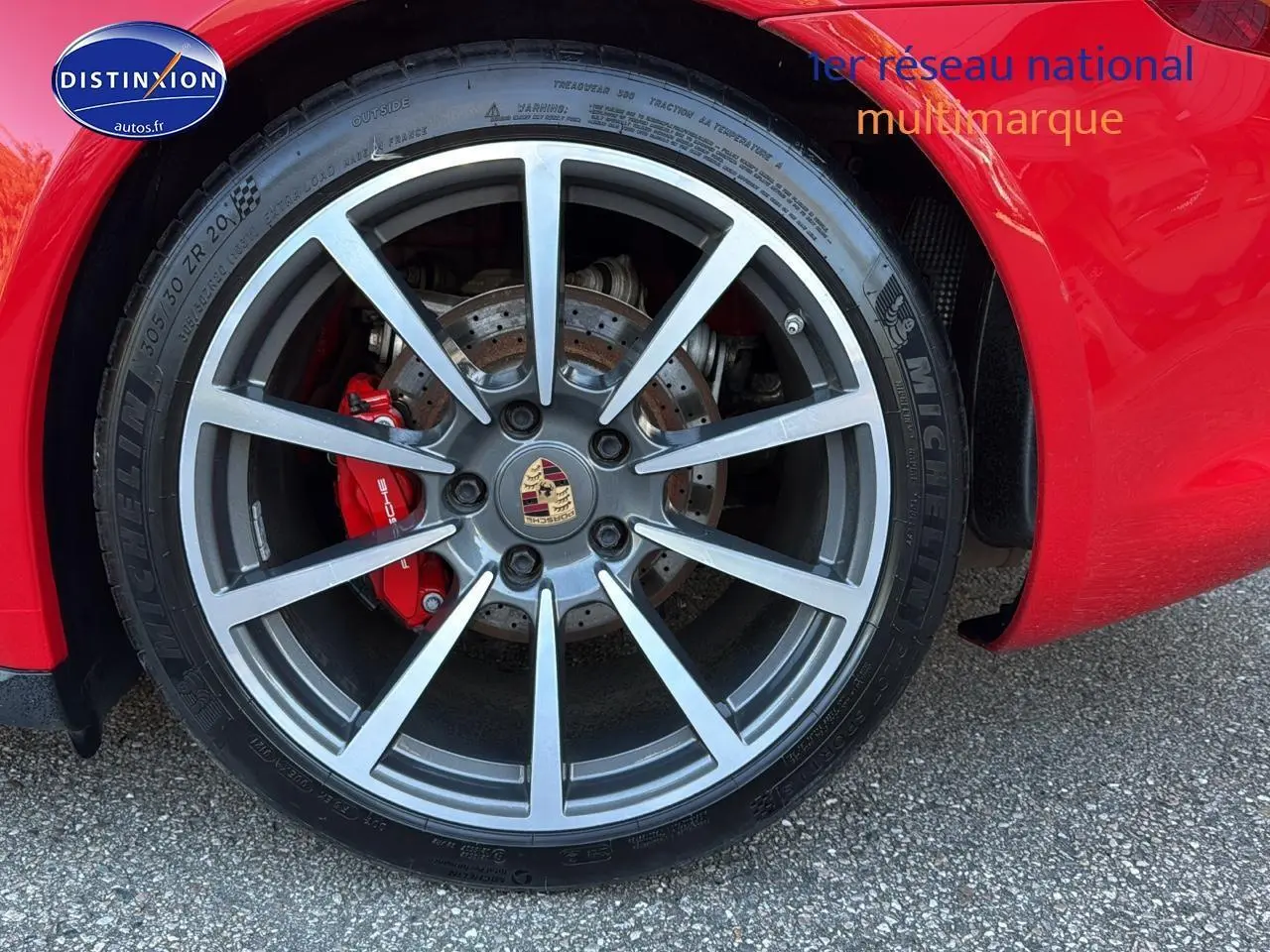 Gros plan sur la jante alu grise et le frein rouge d’une Porsche 911 (991) Carrera 4 PDK rouge.