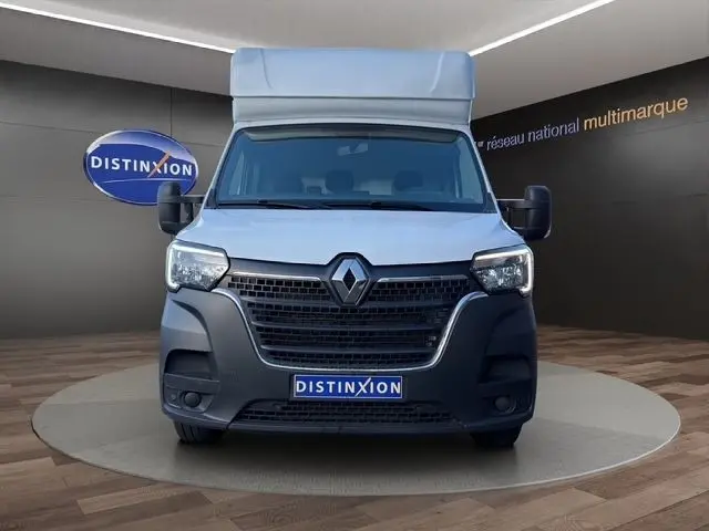 Vue frontale d’un Renault Master blanc avec calandre noire et logo distinctif, présenté en showroom intérieur.