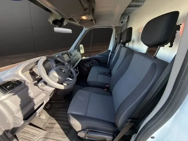 Vue intérieure côté conducteur du Renault Master blanc 2023, montrant les sièges tissu gris et le tableau de bord moderne.