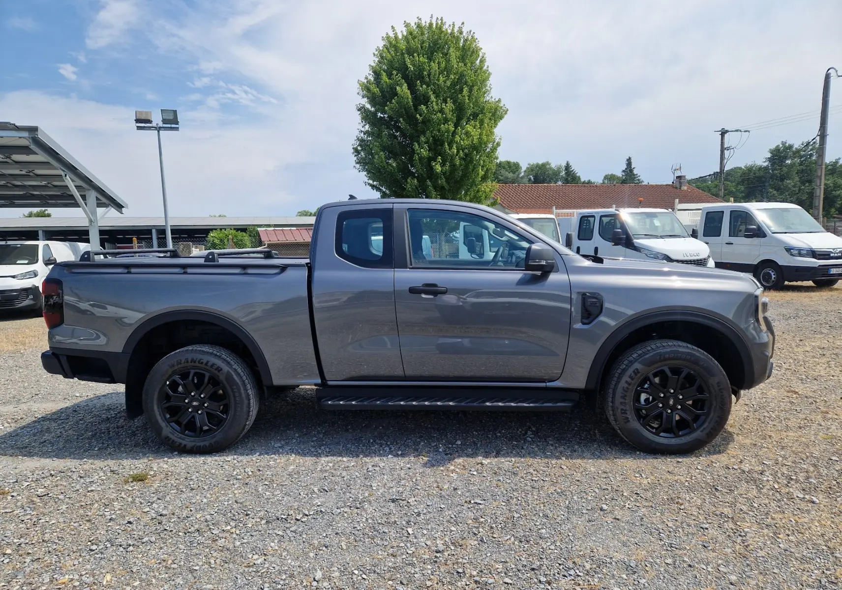 Vue latérale droite d'un Ford Ranger Super Cabine gris carbone avec marchepied et rideau de plateau rigide.