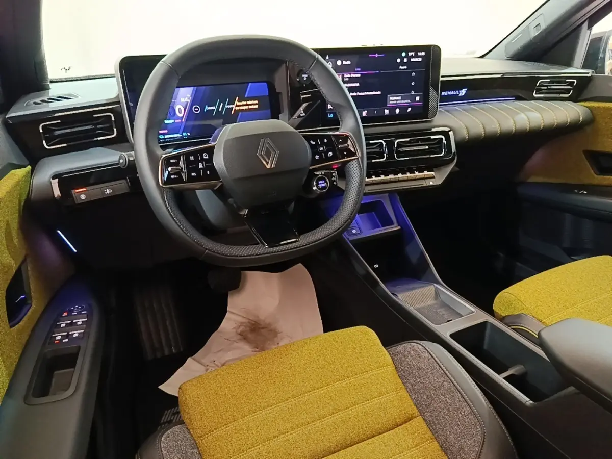 Vue intérieure avant de la Renault R5 électrique 2024, sièges jaunes, tableau de bord avec écran tactile et volant multifonctions.