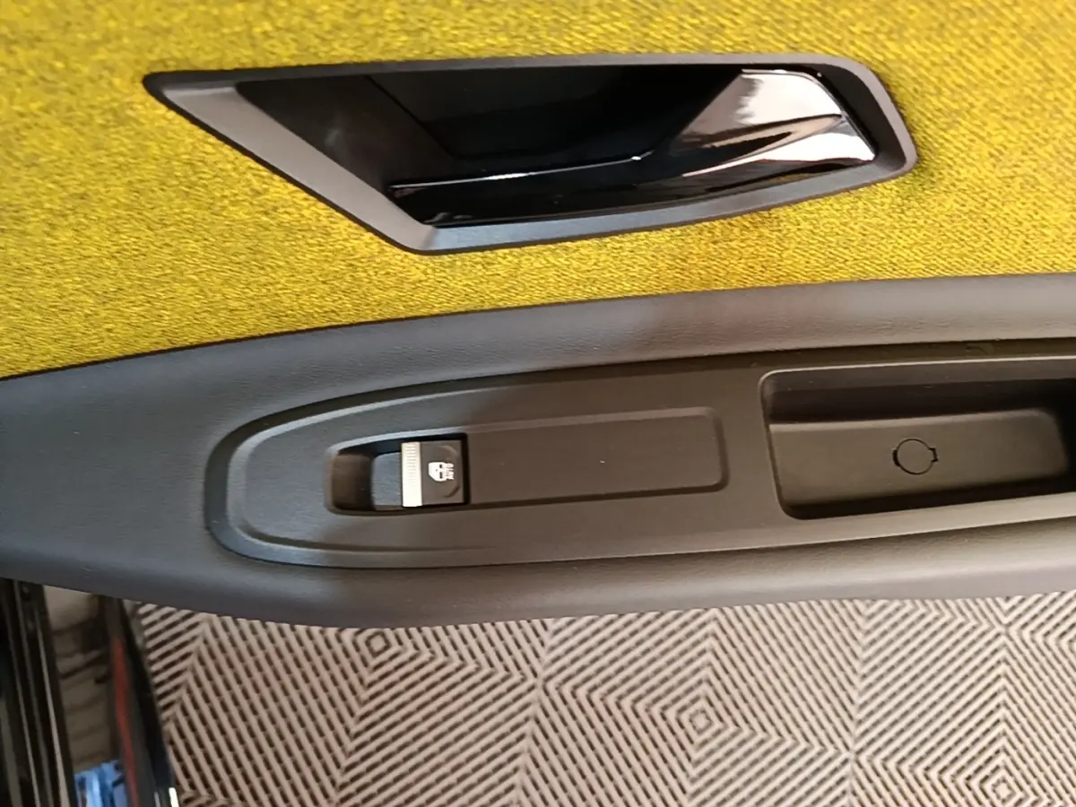 Gros plan sur la poignée intérieure noire et le bouton de verrouillage sur la porte côté gauche avec un revêtement jaune.