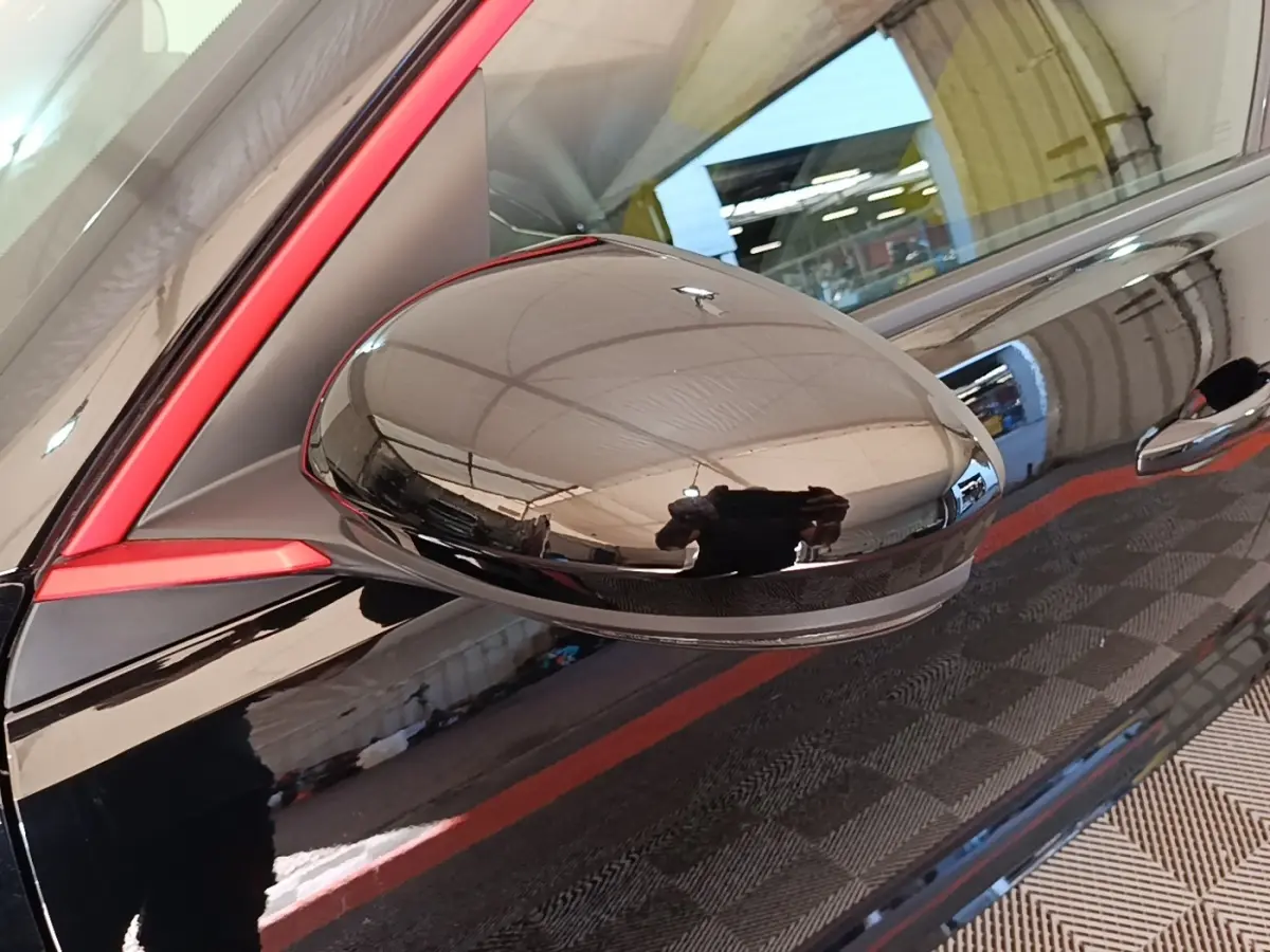 Gros plan sur le rétroviseur côté gauche noir brillant avec cadre rouge d'une Renault R5 électrique 2024.