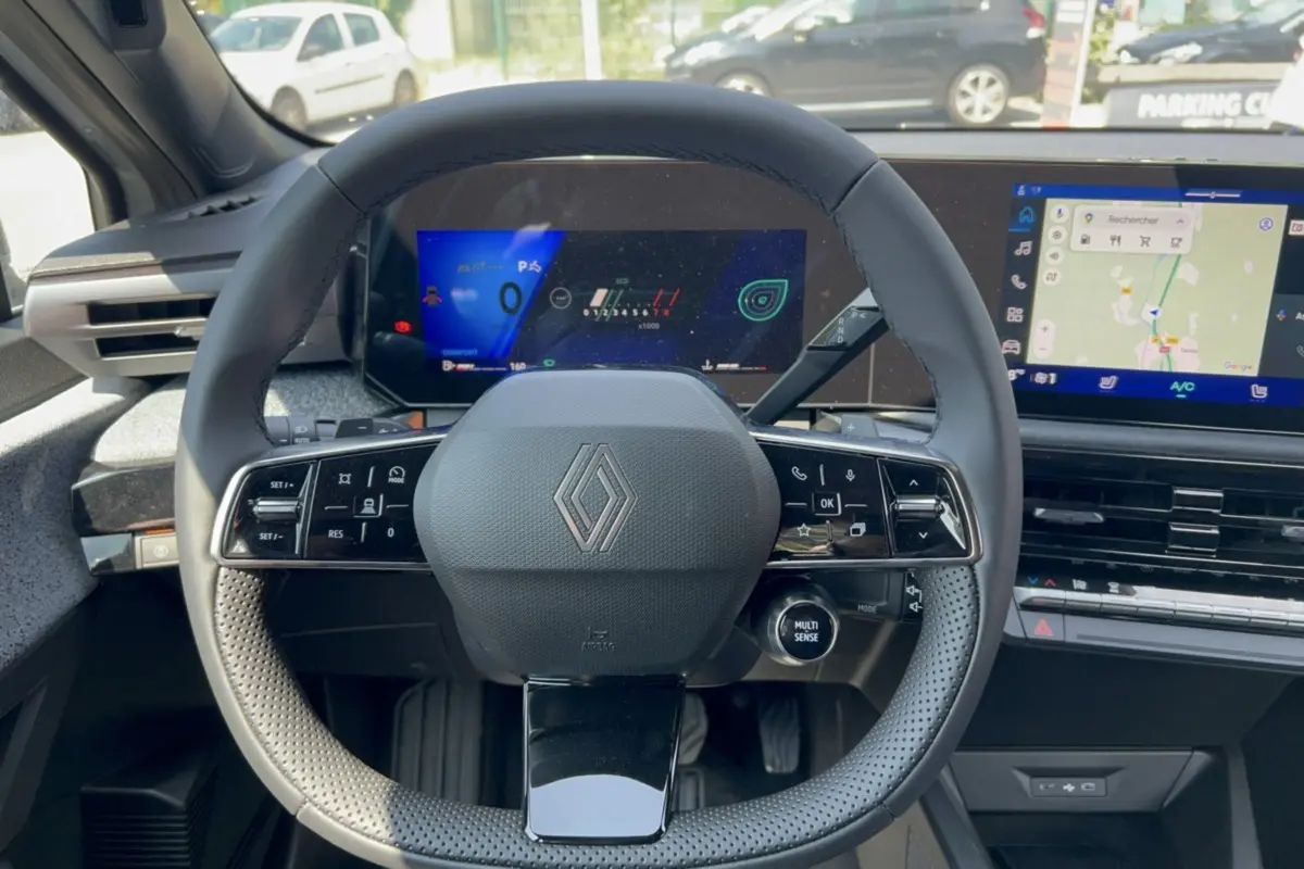 Vue intérieure centrée sur le volant multifonctions de la Renault Clio gris rafale avec tableau de bord numérique et écran tactile.