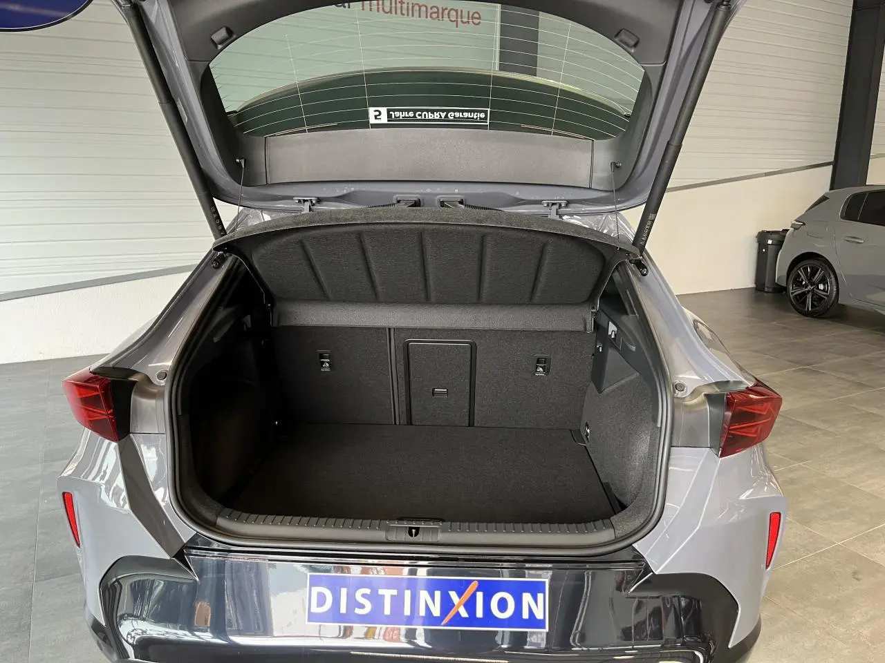 Coffre ouvert d’un CUPRA Formentor gris clair, vue arrière montrant l’espace de chargement et la signature lumineuse arrière.