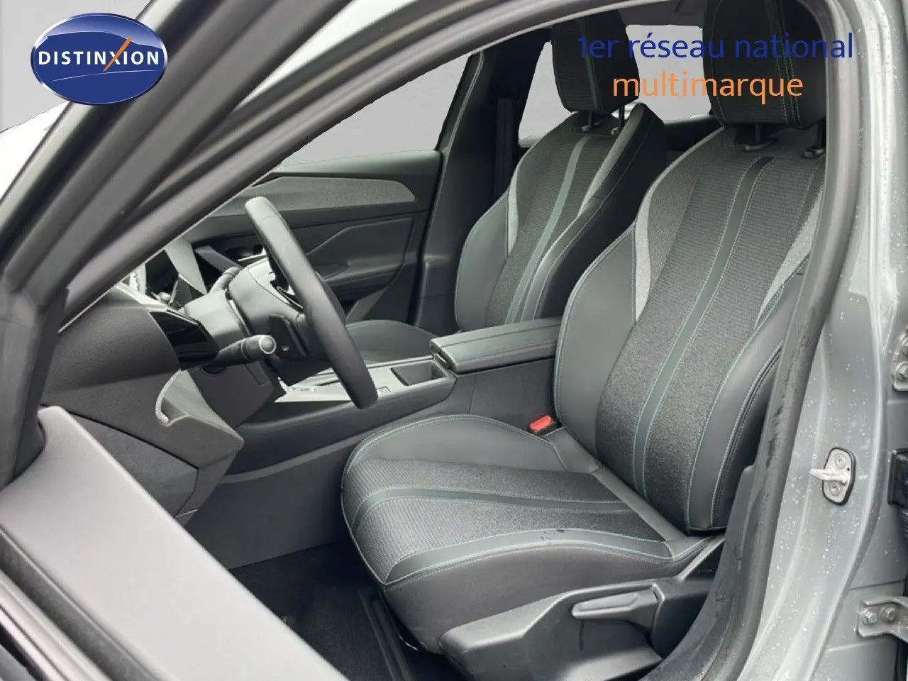 Vue intérieure côté conducteur de la Peugeot 408 gris selenium, montrant sièges tissu et cuir avec surpiqûres bleues.