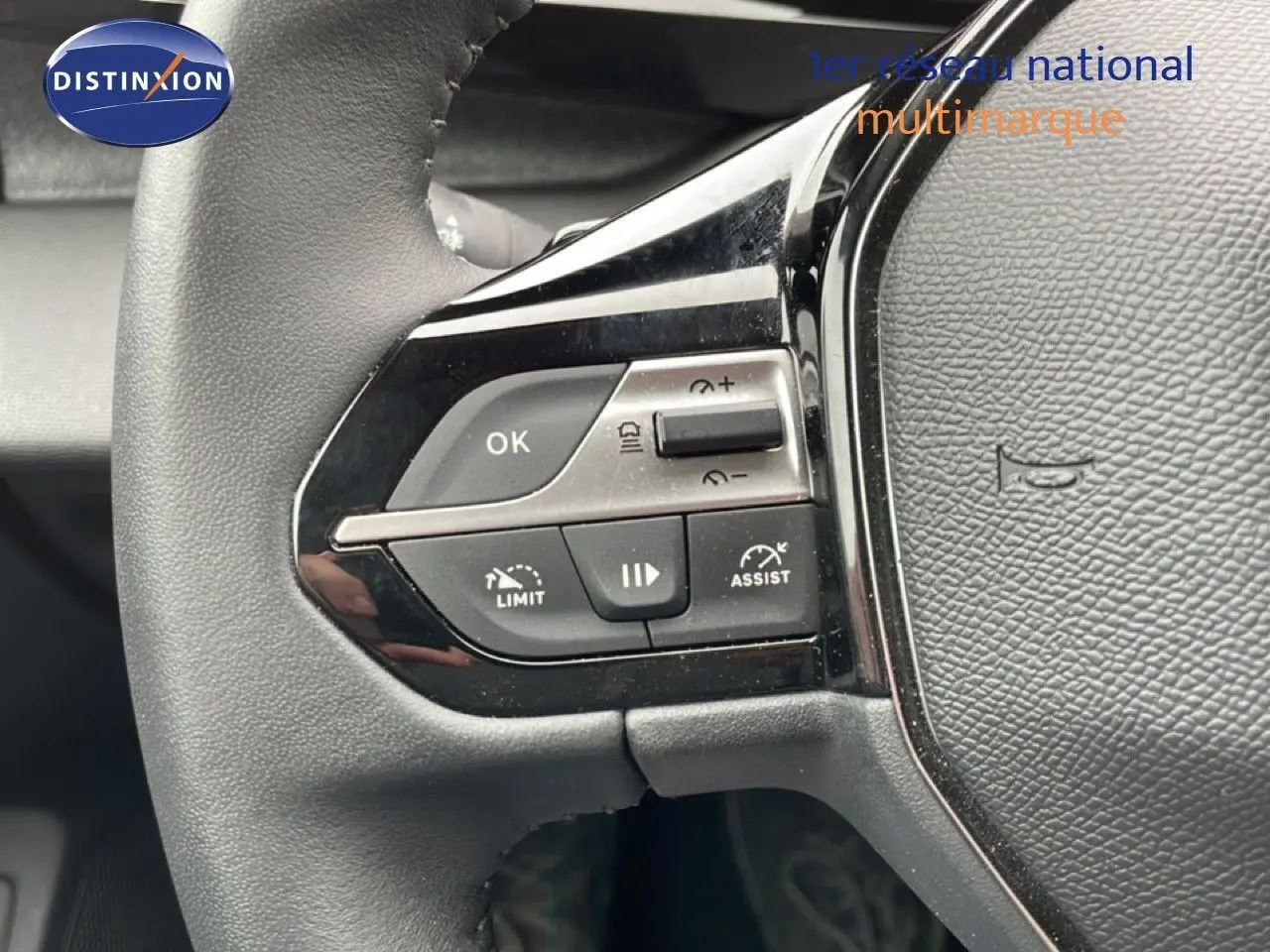 Gros plan sur les commandes du volant noir de la Peugeot 408 1.2 Hybrid 2025, avec boutons de régulateur et limiteur de vitesse.