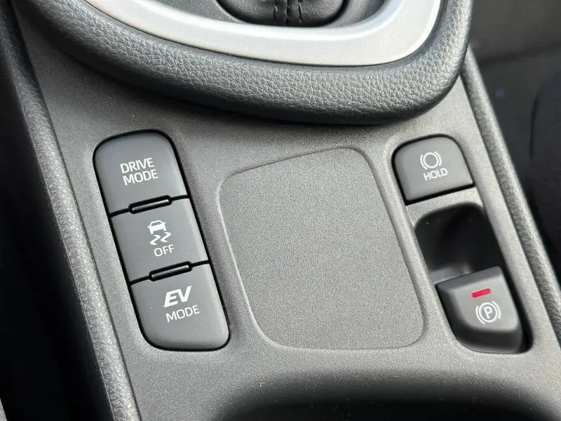 Gros plan sur les boutons de contrôle de conduite et frein à main électronique dans l’habitacle de la Toyota Yaris 116h Dynamic blanc lunaire.