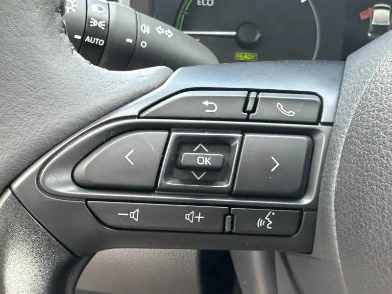 Gros plan sur les commandes multifonctions noires au volant côté gauche de la Toyota Yaris 116h Dynamic blanche 2025.