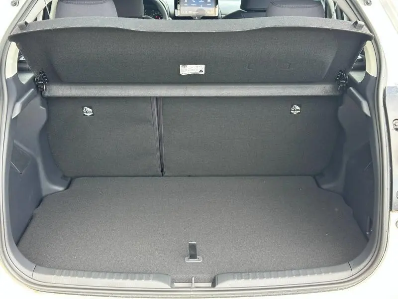 Vue arrière du coffre ouvert de la Toyota Yaris 116h Dynamic 5p MC24 blanc lunaire, montrant l’espace de chargement vide.