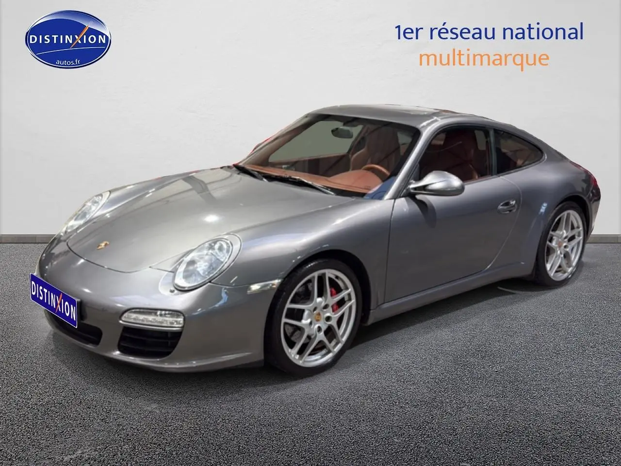 Porsche 911 (997) carrera pdk gris en 3/4 avant droit avec jantes alu et intérieur cuir marron visible.