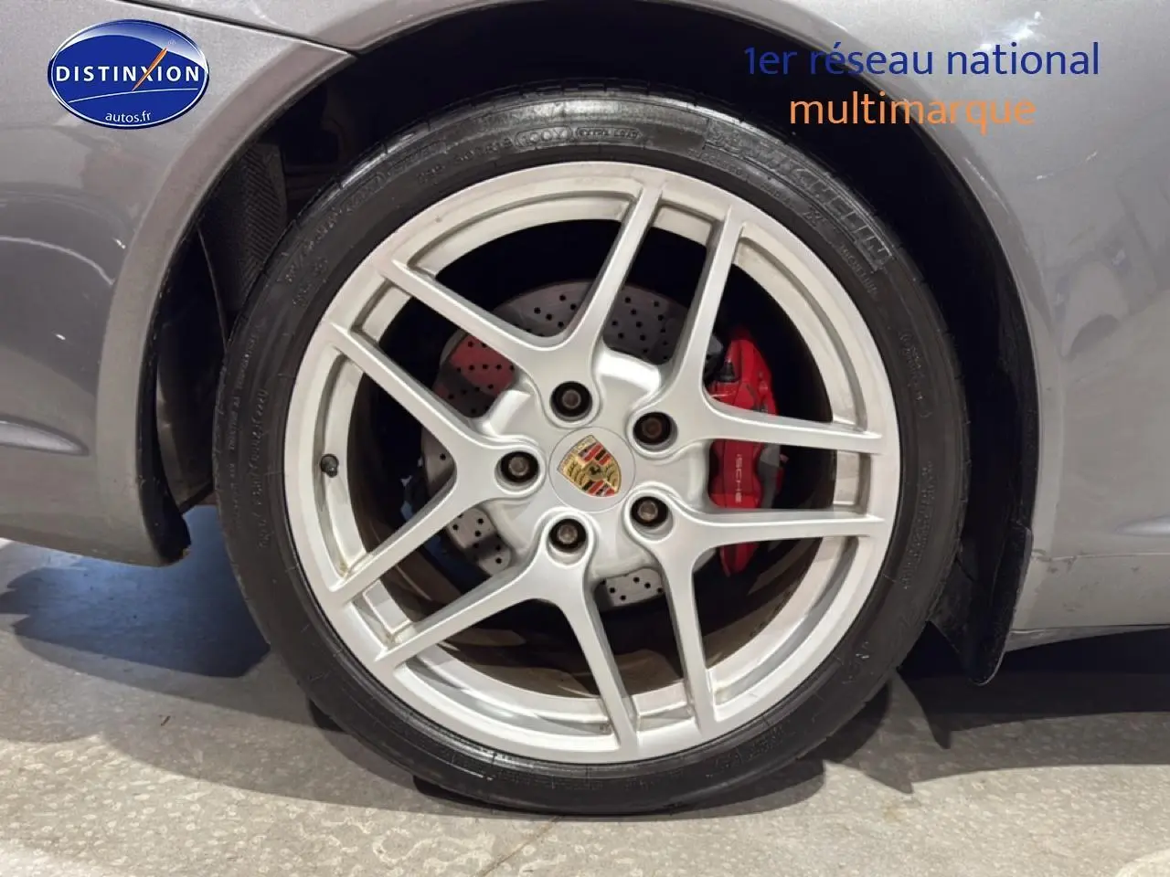 Gros plan sur la jante alu argentée avec logo Porsche et étrier de frein rouge d'une Porsche 911 gris.